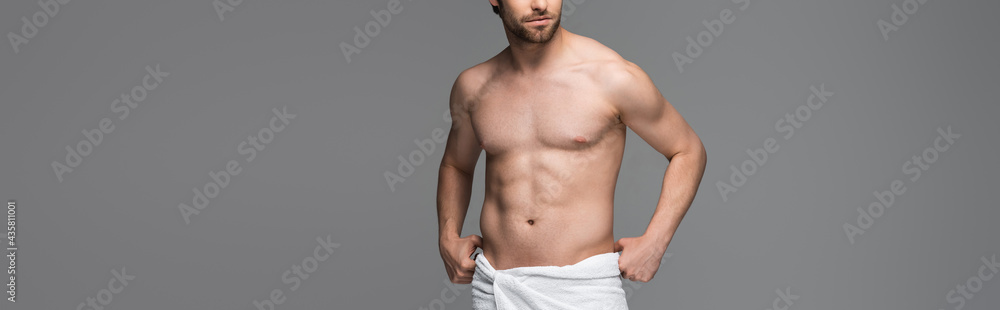 cropped view of shirtless man adjusting towel and standing isolated on grey, banner.