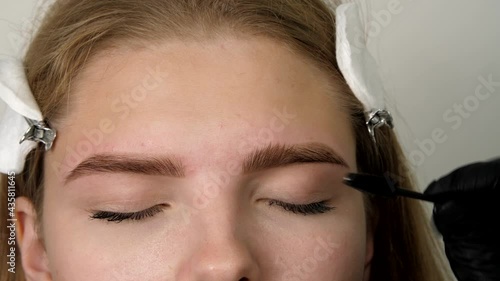 Stylist's hands combing patient’s eyebrows with a special brush before plucking. Gloved master shaping eyebrow with a cosmetic brush close-up. Beautiful attractive female face 