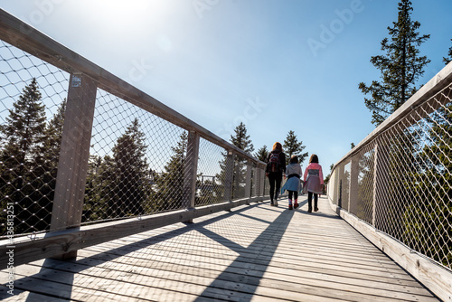 Family people walking wooden treetop bridge canopy walkway in winter.