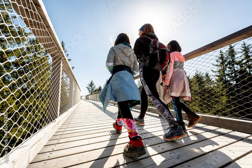 Family people walking wooden treetop bridge canopy walkway in winter.
