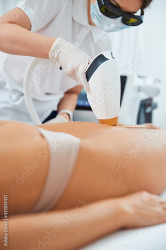 Professional dermatologist performing laser hair removal on patient legs