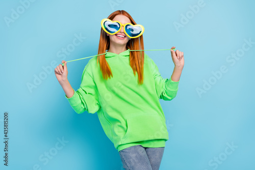 Photo of playful pretty young woman wear green sweatshirt funny heart eyewear dancing smiling isolated blue color background
