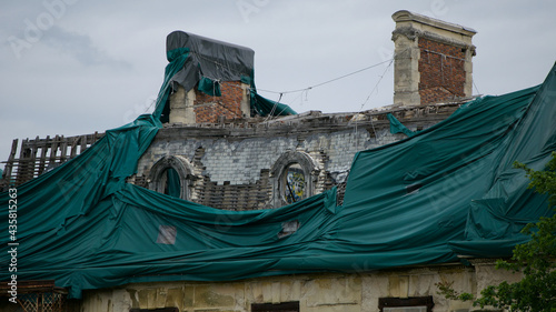 Close-up view of a dilapidated roof of an old building with two chimneys and some tarp laid out as protection