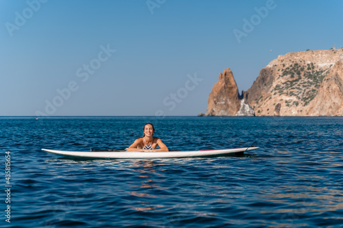 Sporty girl on a glanders surfboard in the sea on a sunny summer day. In a striped swimsuit, he lies on his sap and looks into the frame. Summer activities by Stortom by the sea