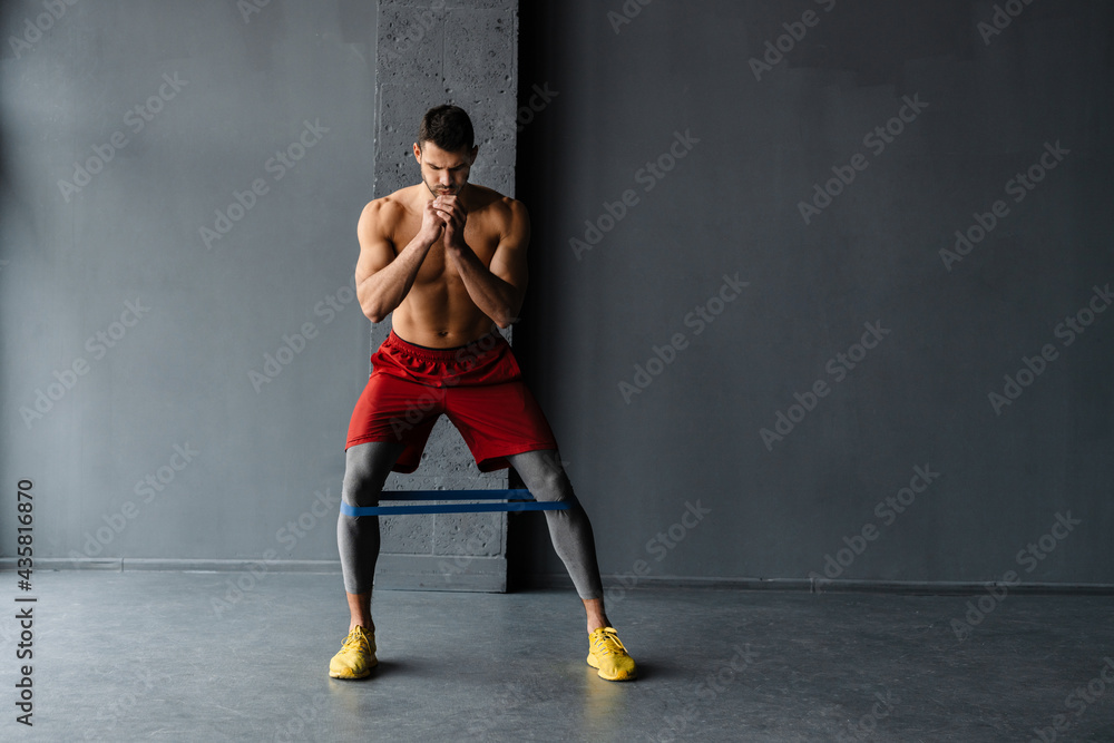 Young shirtless sportsman doing exercise with expander stretch tape Young shirtless sportsman doing exercise with expander stretch tape
