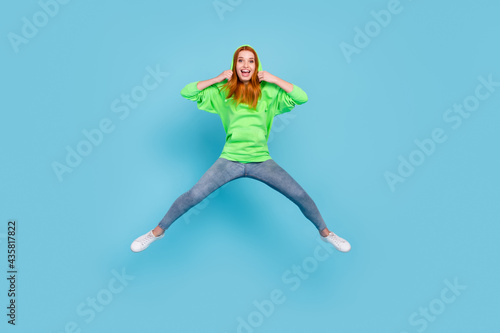 Fototapeta Naklejka Na Ścianę i Meble -  Photo of pretty impressed young lady dressed green hoodie smiling jumping high isolated blue color background