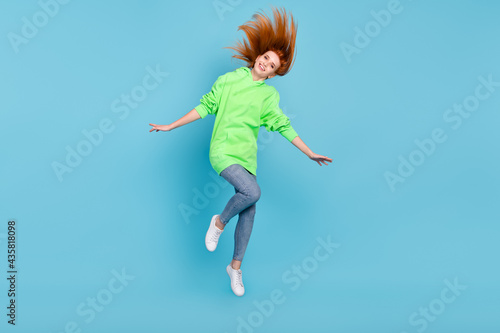 Photo of funky charming young woman wear green sweatshirt jumping high smiling isolated blue color background