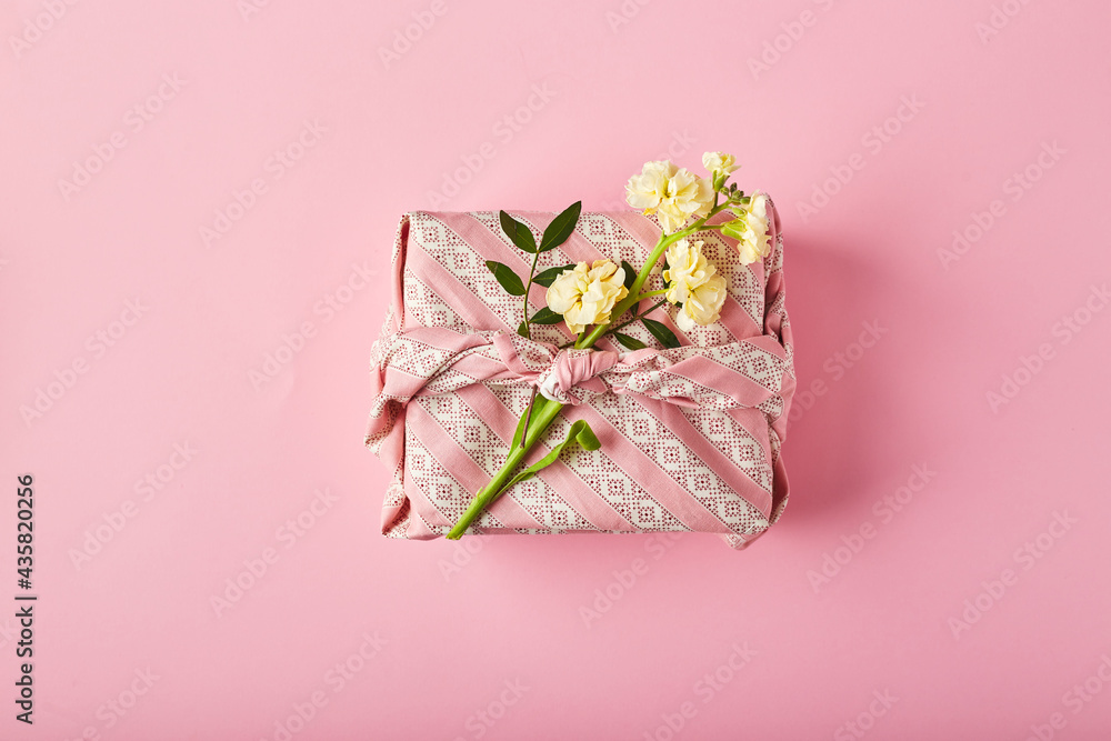 Bouquet of yellow matthiola with gift wrap in traditional japanese furoshiki style. Design concept of holiday greeting on pink table Bouquet of yellow matthiola with gift wrap in traditional japanese furoshiki style. Design concept of holiday greeting on pink table