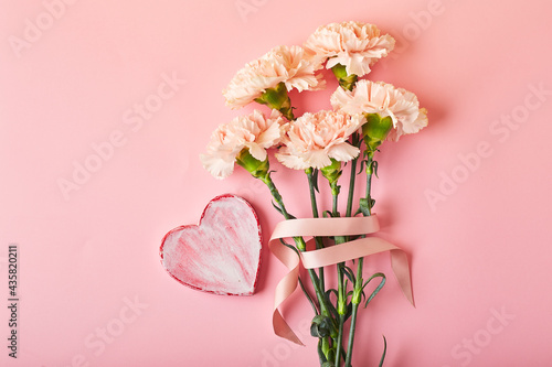 Bouquet of pink carnations and decorative heart. Design concept of holiday greeting with carnation bouquet on pink table background © Irina Burakova