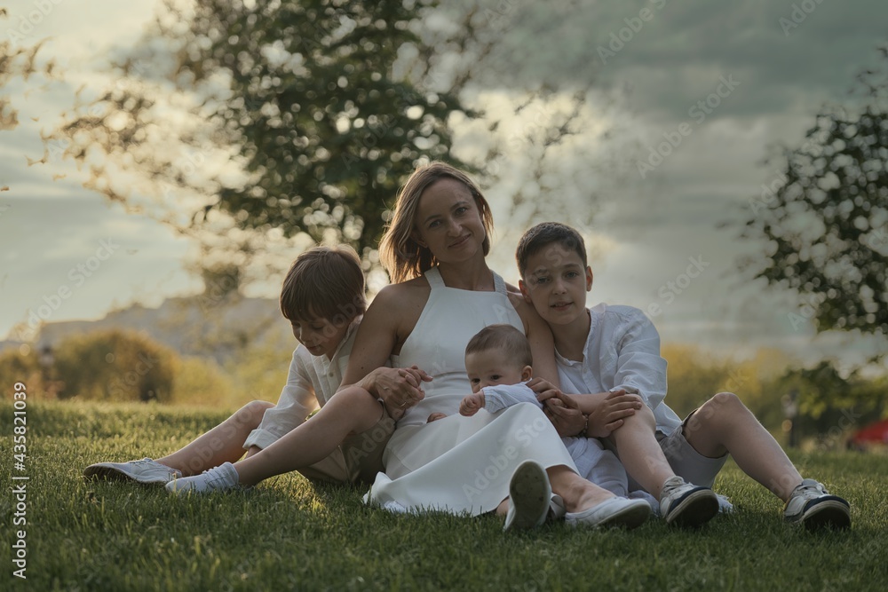 Mother and three children hugging. Happy family sitting outdoor: woman and two brother kids boys and cute little toddler boy Mother and three children hugging. Happy family sitting outdoor: woman and two brother kids boys and cute little toddler boy