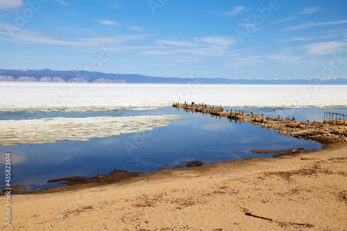 Sandy beach  old ruined wooden pier on the island of Olkhon in the spring. Lake Baikal during the ice drift.