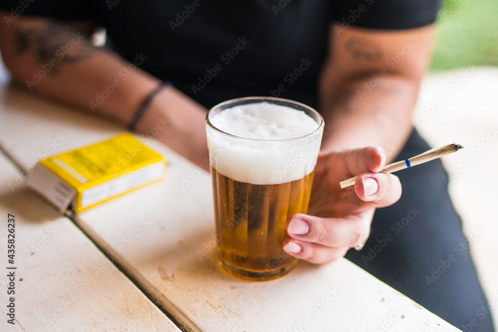 Mulher tomando cerveja em copo americano e segurando um cigarro de