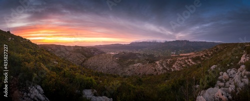 Panoramic of a magical sunset. A sunset lights the mountains orange as clouds cover the top of a mountain. Sunset in Valencia  Spain. Sunset on the mountain