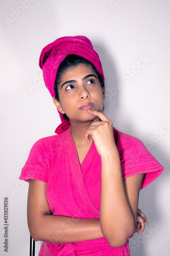 Beautiful Indian Lady in a pink bathrobe after bath giving beauty funny poses in front of the camera with body lotion and cucumber on her face