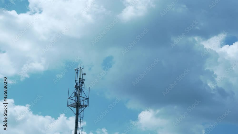 Cell Tower, Mobile Operator Equipment, Tower Of The GSM Mobile Operator on The Background Of Time Lapse Puffy White Clouds in A Blue Clear Sky Sunny Weather In The Afternoon. Cell Tower, Mobile Operator Equipment, Tower Of The GSM Mobile Operator on The Background Of Time Lapse Puffy White Clouds in A Blue Clear Sky Sunny Weather In The Afternoon.