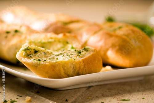 Sliced baguette bread with herb butter on plate, close-up
