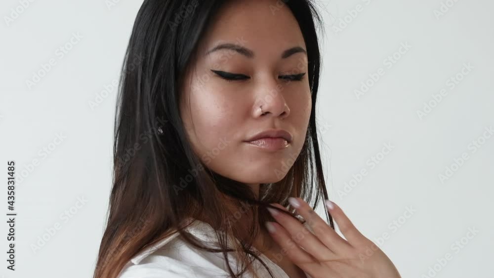 Stylish trend look. Beautiful asian woman. Fashion model. Casual makeup. Confident brunette lady with black eyeliner pastel lipstick classic white shirt isolated light slow motion.