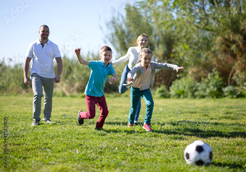 Father with mother with two children enjoy playing soccer on lawn in summer park © caftor