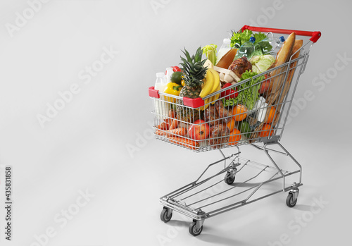 Shopping cart full of groceries on grey background. Space for text photo