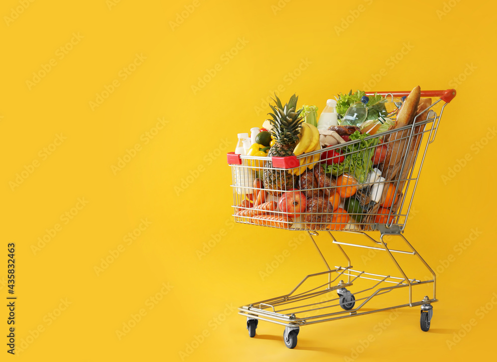 Shopping cart full of groceries on yellow background. Space for text - obrazy, fototapety, plakaty 