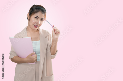An Asian woman with a smiling face standing with a book and a pen.