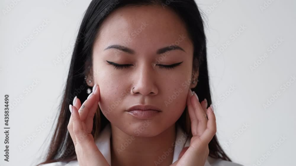 Face contouring. Lifting massage. Female beauty care. Rejuvenation treatment. Pretty asian woman touching forehead zone by hand applying anti-aging cosmetic isolated white. Face contouring. Lifting massage. Female beauty care. Rejuvenation treatment. Pretty asian woman touching forehead zone by hand applying anti-aging cosmetic isolated white.