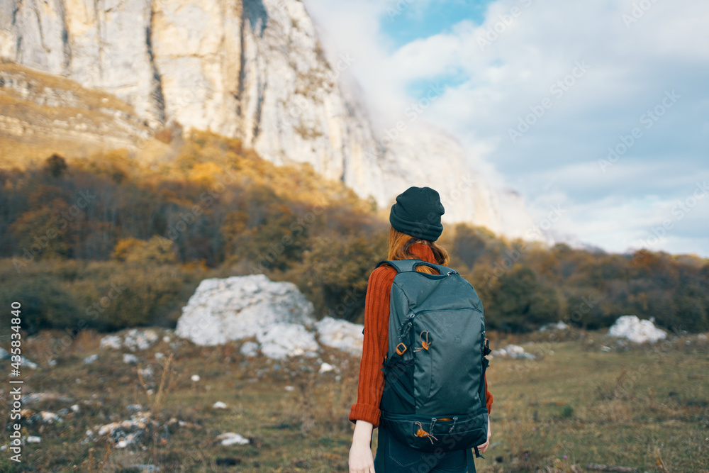 a traveler in a sweater and a hat is resting in the mountains in nature and a backpack on her back