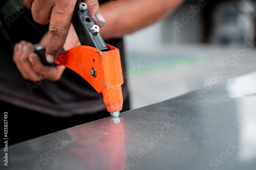 Man's hand is working with a rivet gun and a piece of zinc and steel photo