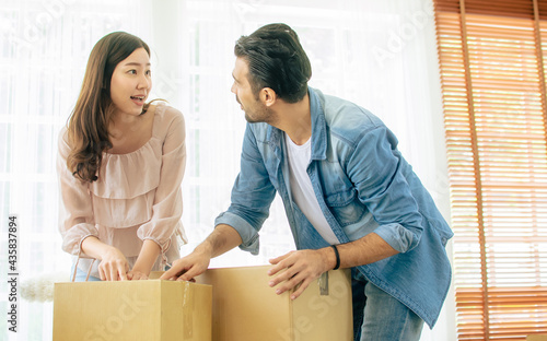Mixed race Asian Caucasian adorable cute couple helping each other to move new house, carrying and arranging carton paper unpacking boxes with happiness and warmth. Investment and Real Estate Concept. © Ann Rodchua