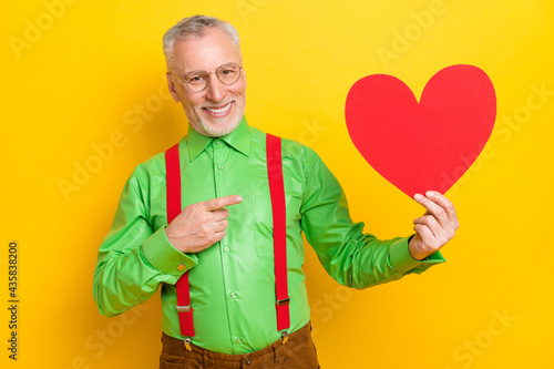 Photo of aged man happy positive smile point finger paper heart advert suggest promo isolated over yellow color background