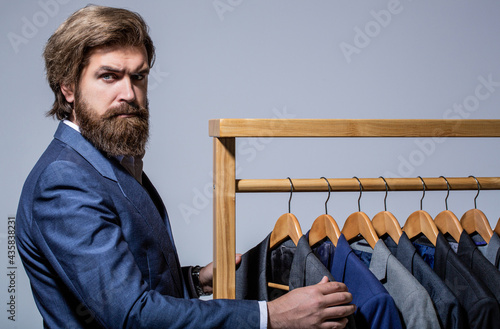 Tailor, tailoring. Stylish men's suit. workshop. Handsome bearded fashion man in classical costume suit. Male suits hanging in a row. Men clothing, boutiques. Man suit, tailor in his photo