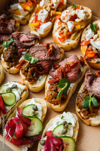
A set of different snacks for a party or a festive table. Ciabatta sandwiches with tomatoes, jamon, cream cheese, vegetables, chambers and olives. Delicious wine snacks
