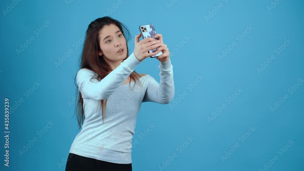 The young blogger takes selfies for a story on instagram. Asian with dark hair, dressed in a blue blouse, isolated on a dark blue background in the studio. The lifestyle concept of sincere emotions The young blogger takes selfies for a story on instagram. Asian with dark hair, dressed in a blue blouse, isolated on a dark blue background in the studio. The lifestyle concept of sincere emotions