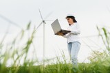 Close up portrait of female engineer in helmet standing and using laptop computer while checking the work of windmill tourbine at renewable energy station.