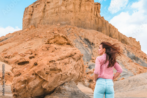 A young woman stands near a huge boulder with a beautiful view of Alstrom Point, Utah, USA
