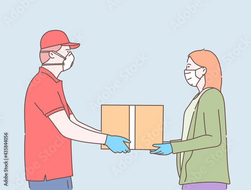 Online safe delivery service concept. Young courier man with medical mask delivering a package or box to woman during coronavirus quarantine © Vadim