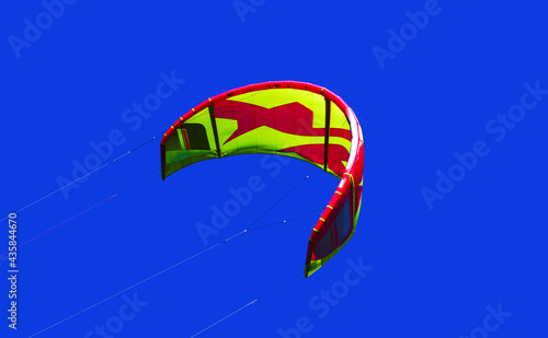 Beautiful kite, wind-curved kitesurfing parafoil flying in the blue sky. The slings are tight. Ripstop nylon, a flexible and durable curved wing. Flight over water.