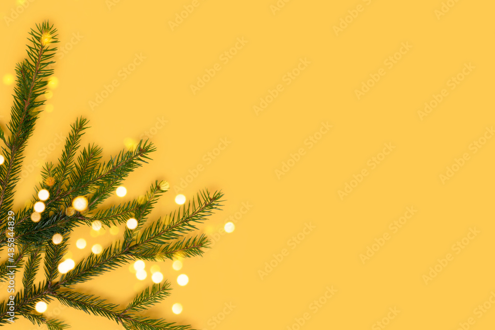 Fir branch and golden bokeh on a yellow background. New Years composition with place for text.