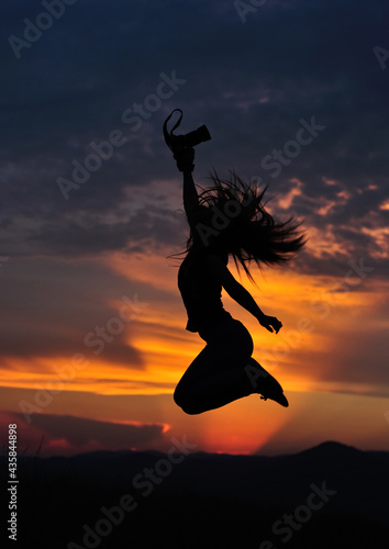 Girl silhouette jumping with photo camera in hand in sunset. Low key shot.