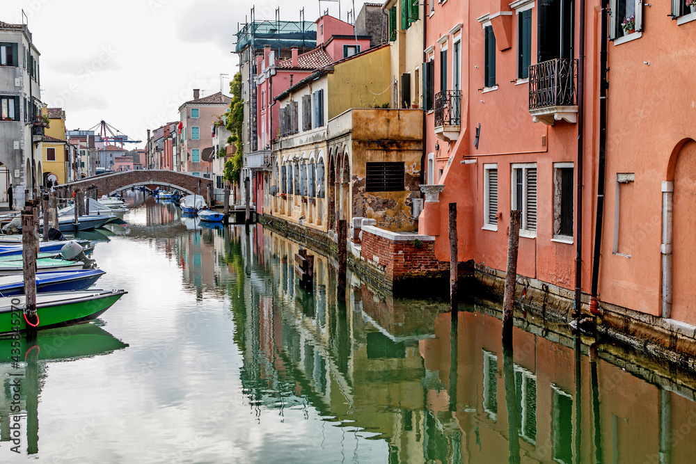 Colorful houses of the ancient city of Chioggia, Venice lagoon, reflected in the water with boats and stone bridges 