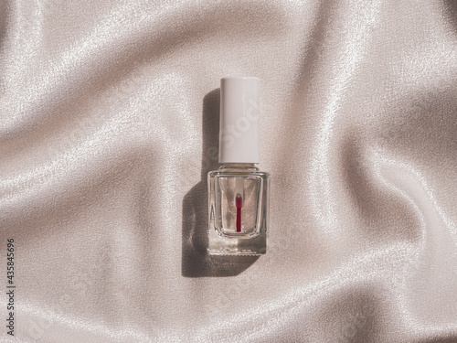 Nail polish bottle mockup with harsh shadow on white silk background french manicure cosmetics product. Sparkling transparent nailpolish against delamination cracking make-up. Design branding template photo