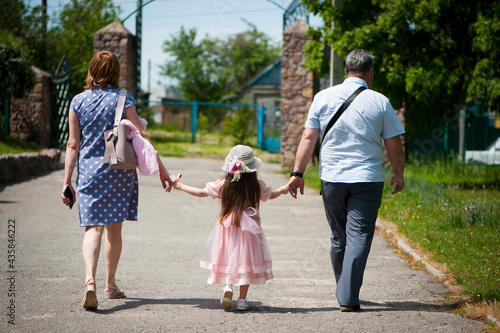 family walking in the park. mom dad and little girl walking holding hands. back view. daughter in a pink dress. friendly loving family concept, love. outdoor, walk in the fresh air, threesome
