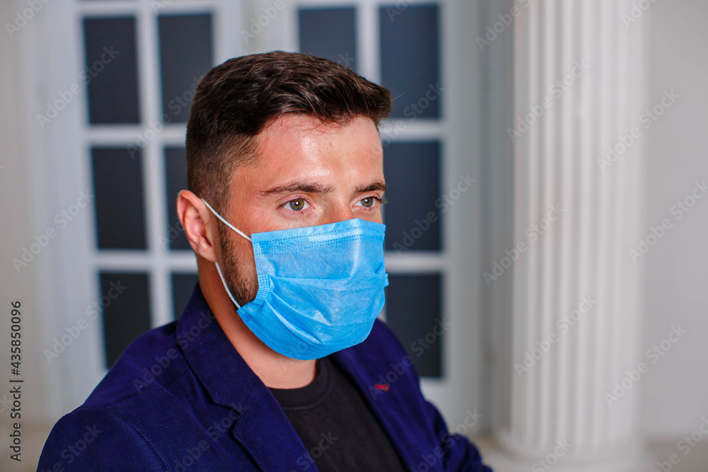 Portrait of a handsome young businessman with a surgical medical mask. Business people medicine and healthcare concept. Indoor, studio shot on blue background