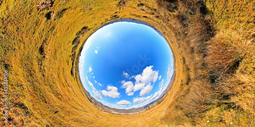 Panorama of a late winter field in full sun with very blue sky and white clouds. Stereographic panoramic projection