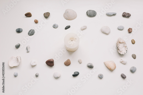 White candle and seashells and stones on white background. Spa concept. Flat lay, top view