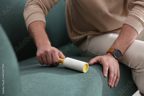 Man cleaning sofa with lint roller indoors, closeup photo