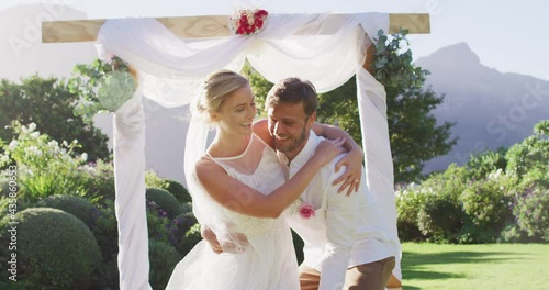 Happy caucasian husband carries newly wed bride and walks down altar outdoors