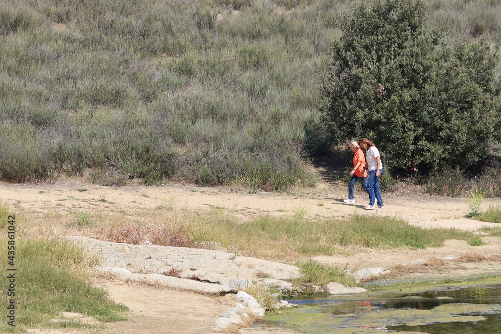 Mother and Daughter on a Walk on a Dry California Hill Trail Next to a Recreational Lake