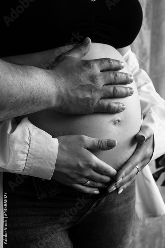 Parents' hands lie on the belly of the pregnant woman. Young parents expecting a baby