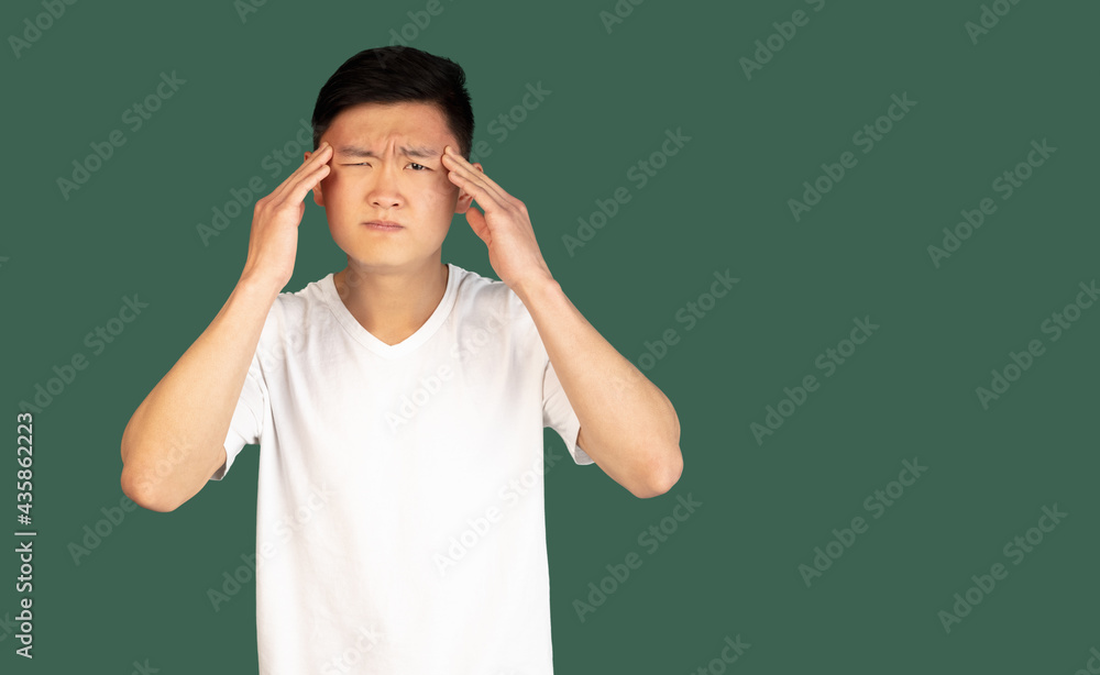 Asian young man's portrait on green studio background. Concept of human emotions, facial expression, youth, sales, ad. Asian young man's portrait on green studio background. Concept of human emotions, facial expression, youth, sales, ad.